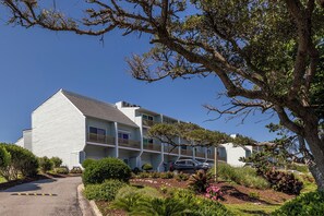 A multi-story building with a sloped roof, balconies, and a parking area. - Coral Shores #12 - Oceanfront Condo (Pine Knoll Shores)