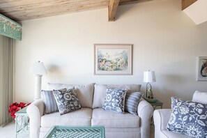 A living room with a sofa, two side tables, a framed picture, and a lamp. - Coral Shores #12 - Oceanfront Condo (Pine Knoll Shores)
