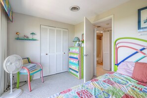 Ein Schlafzimmer mit Bett, Stuhl, Ventilator, Kleiderschrank und einer Badezimmertür.