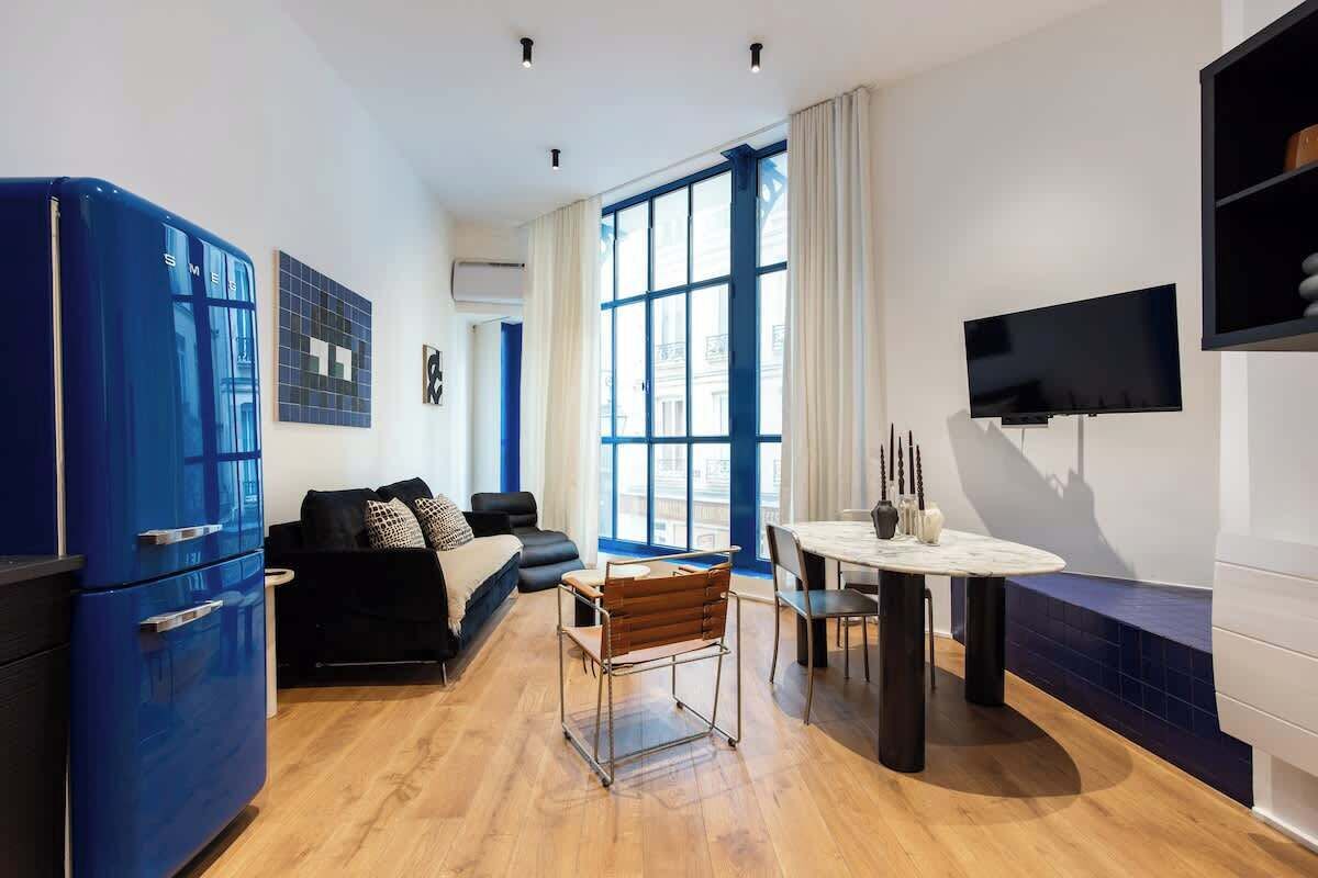 Un espace de vie compact comprenant un coin cuisine, un coin repas, un canapé et un téléviseur fixé au mur.