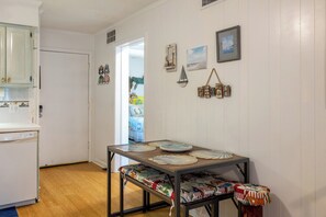 A dining area with a table set for four, a bench, and a view of a beach through an open door. - Southwinds A9 - 2 Bedrooms, 1.5 Baths, Oceanfront Condo (Atlantic Beach)