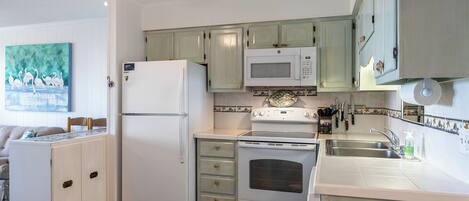 A compact kitchen with a refrigerator, microwave, stove, and sink.