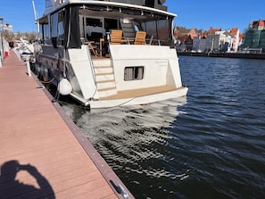 Un bateau blanc était amarré à un quai, doté d’une zone de pont couverte et d’espaces pour s’asseoir.