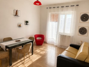 Un salon moderne comprenant un coin repas, un fauteuil rouge, un canapé noir et une suspension rouge.
