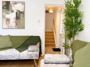 Un salon avec un canapé, une plante verte et un escalier menant à une autre pièce.