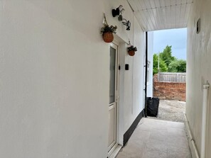 Un couloir aux murs blancs, doté d’un sol carrelé et agrémenté de suspensions florales.