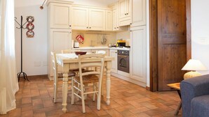 A kitchen with white cabinets, a dining table with chairs, a stove, and a wooden door. - Nice apartment for 4 people with WIFI, pool, A/C, TV, patio and pets allowed (Panicale)