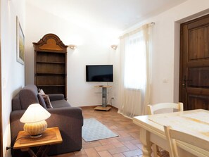 Ein Wohnzimmer mit einer Couch, einem Tisch, einer Lampe, einem Fernseher und einem Bücherregal.