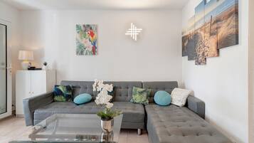 Ein Wohnzimmer mit einem grauen Sofa, einem Glastisch und einer Topfpflanze.