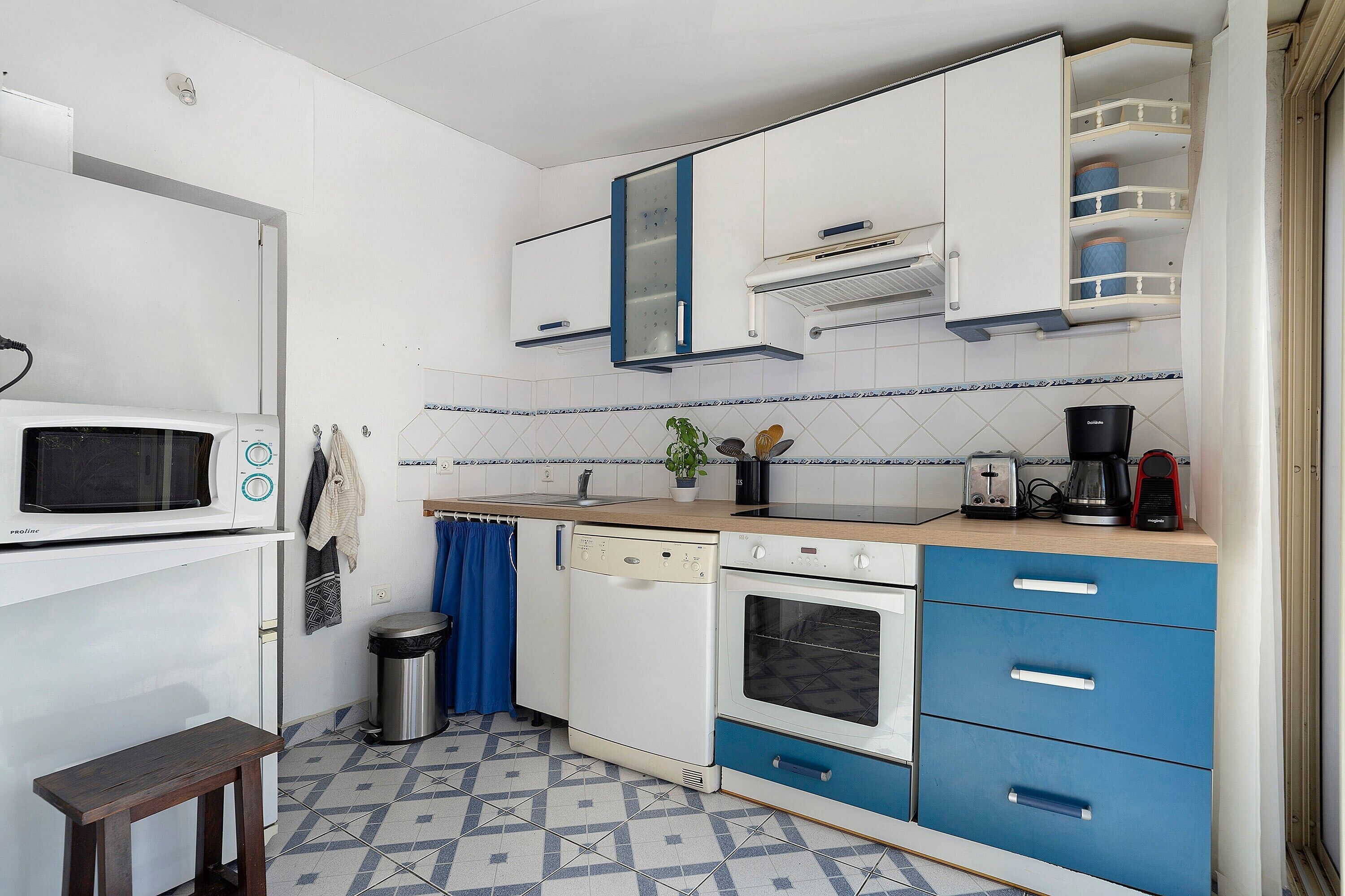 A compact kitchen with white and blue cabinets, a microwave, a stove, and a toaster.