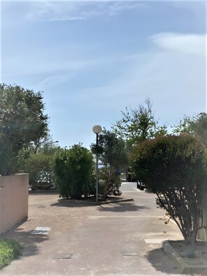 A paved pathway flanked by greenery, a street lamp, and a clear sky.