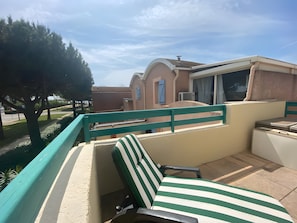 A balcony with a green-striped chair, a view of a building with a blue door, and a tree.