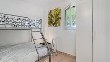 A bunk bed with a patterned mattress, a radiator, a window with a view of greenery, and a white wardrobe.