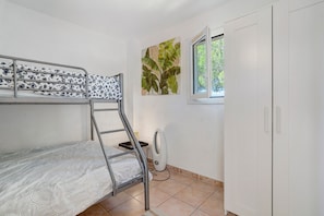 A bunk bed with a patterned mattress, a radiator, a window with a view of greenery, and a white wardrobe.