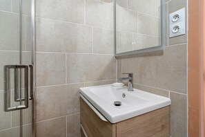 A bathroom with a white sink, a mirror, and a shower area. - Villa 80m from Grazel Beach – Wifi, Parking, Sleeps 7 (Gruissan)