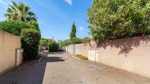 Un estrecho callejón con un sendero de grava, bordeado por muros con vegetación y un árbol alto.