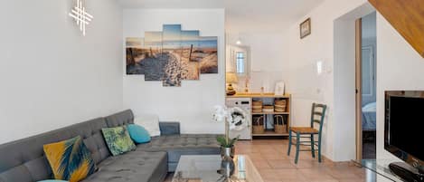 A living room with a grey sofa, a glass coffee table, and a painting of a beach scene.