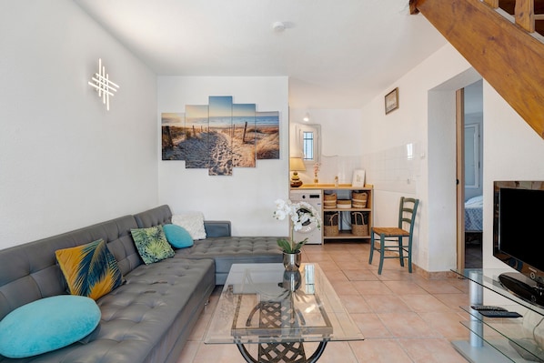 A living room with a grey sofa, a glass coffee table, and a painting of a beach scene.