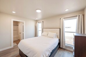 A bedroom with a bed, a wardrobe, a window with curtains, and a ceiling light. - The Jade - Cozy Lubbock Getaway - Sleeps 6 (Lubbock)