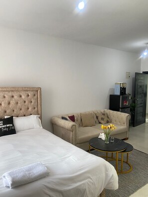 Ein Hotelzimmer mit einem großen Bett, einer Couch, einem kleinen runden Tisch mit Blumenvase und einer Kaffeemaschine.