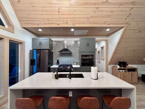 A modern kitchen with a central island, grey cabinets, and a stainless steel range hood. - Luxury Couples or Family Cabin/Hot Tub/Fire Pit (Broken Bow)