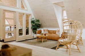 Ein Loft-Zimmer mit hohen Decken, Holzboden, einer Couch, einem runden Holztisch und einem Korbstuhl.