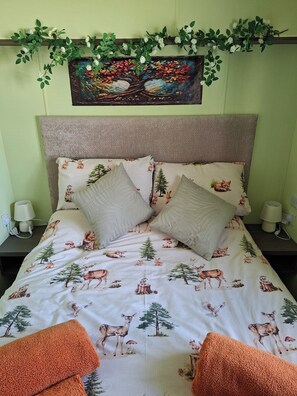 Ein Bett mit einem Bettbezug mit Waldmotiv, zwei Kissen und einem Kopfteil.