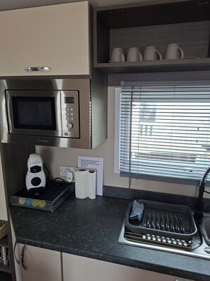 Eine KĂŒchenzeile mit Mikrowelle, Kaffeemaschine und einem Fenster mit Jalousien.