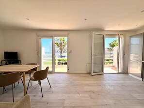Un salon moderne comprenant une table à manger, des chaises, un téléviseur et des portes-fenêtres coulissantes donnant sur un balcon avec vue sur des palmiers et des immeubles.