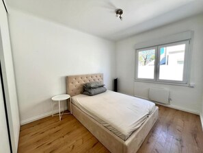 Une chambre à coucher avec un lit, une petite table ronde, une fenêtre et un radiateur.