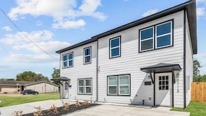 A two-story residential building with a driveway, a covered porch, and a fenced yard. - Reed Unit B - Home & Private Rooms (Houston)