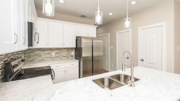 A modern kitchen with white cabinets, stainless steel appliances, a marble countertop, and pendant lighting. - Reed Unit B - Home & Private Rooms (Houston)