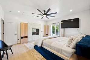 Ein Schlafzimmer mit einem Bett, einem Deckenventilator, einem Fernseher und einem großen Fenster.