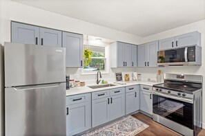 A modern kitchen with grey cabinets, stainless steel appliances, a window with a view, and a patterned rug. - Cozy up in The Book Nook 2 - minutes from downtown Chesterton and Indiana Dunes (Chesterton)
