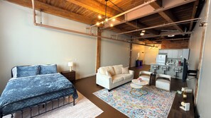 A bedroom with a bed, a sofa, a small table, and a kitchen area with a fridge and bar stools. - Freshly renovated Studio Loft in the heart of Corktown. (Detroit)