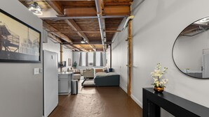 A hallway with exposed wooden beams, a bed, a desk, and a mirror on the wall. - Freshly renovated Studio Loft in the heart of Corktown. (Detroit)