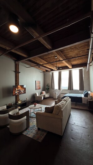 A spacious living area with a high ceiling, exposed beams, a fireplace, and a large window with curtains. - Freshly renovated Studio Loft in the heart of Corktown. (Detroit)