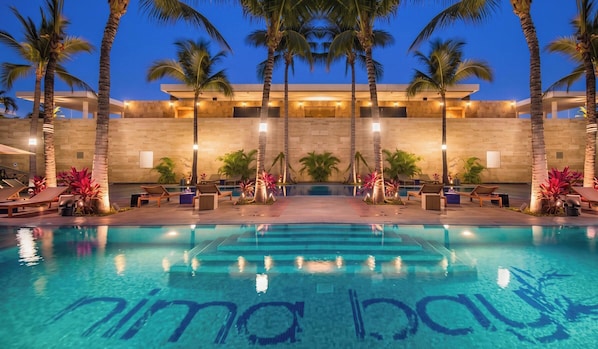 A pool with 'Nima Bay' written on the water, surrounded by palm trees and lounge chairs.