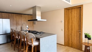 Une cuisine moderne dotée d’un îlot central, de tabourets de bar, d’une hotte en acier inoxydable et d’une porte en bois.