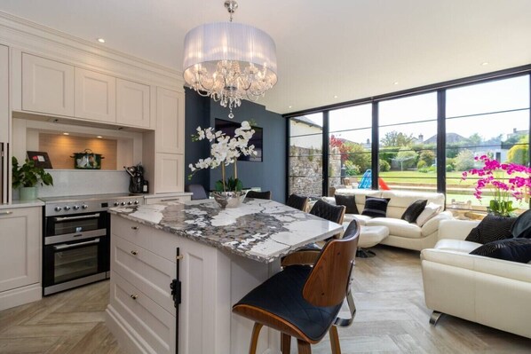 A modern kitchen with a marble island, built-in oven, and a dining area with a white sofa and chairs.