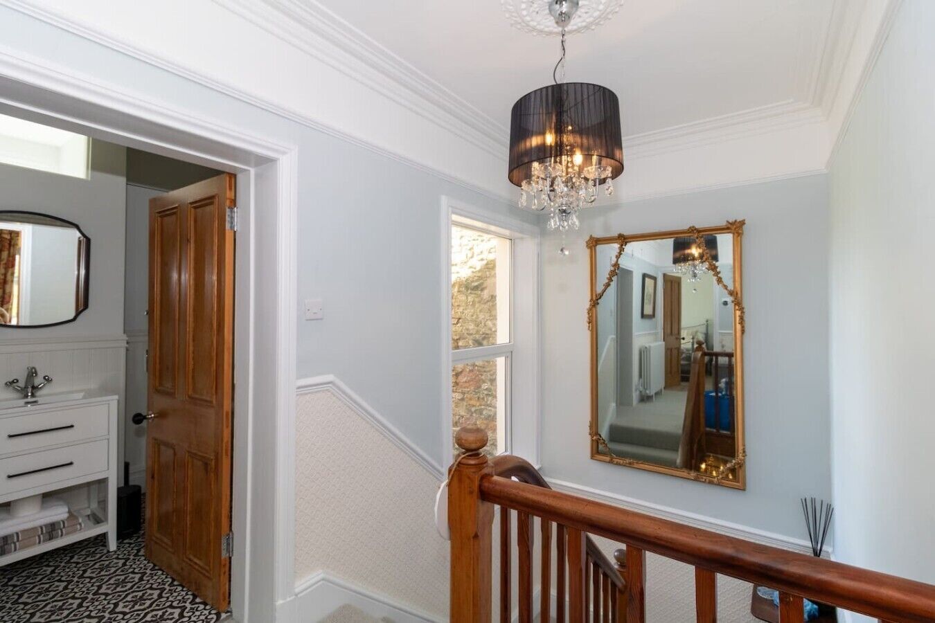 A hallway with a staircase, a chandelier, a mirror, and a door leading to a bathroom.