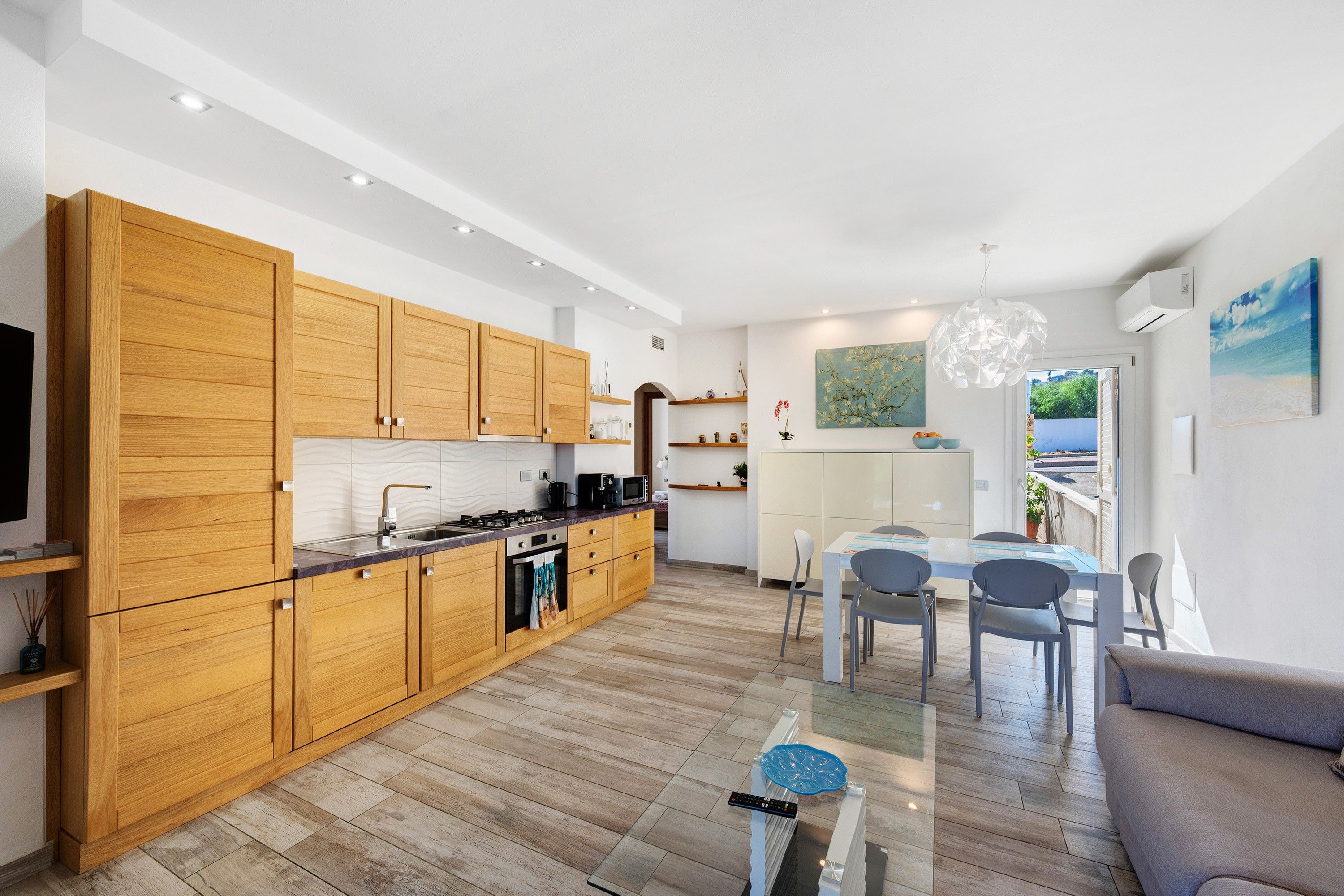 Eine moderne Küche mit Holzschränken, ein Essbereich mit einem Glastisch und ein Wohnzimmer mit einer Couch.