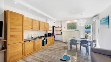 Eine moderne Küche mit Holzschränken, ein Essbereich mit einem Glastisch und ein Wohnzimmer mit einer Couch.