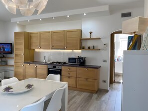 A modern kitchen with wooden cabinets, a microwave, a stove, and a dining area with a white table and chairs. - R House II: Your Paradise Retreat in Budoni (Budoni)