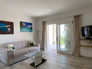 A modern living room with a sofa, a glass coffee table, a flat-screen TV, and a sliding glass door leading to an outdoor area. - R House II: Your Paradise Retreat in Budoni (Budoni)