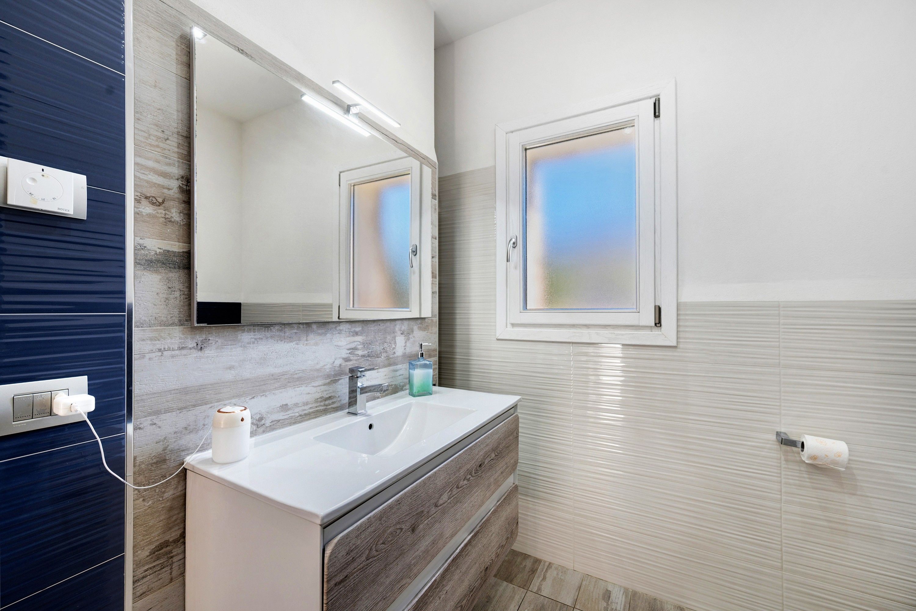 Een moderne badkamer met een witte wastafel, een spiegel en een etsbeglazing.