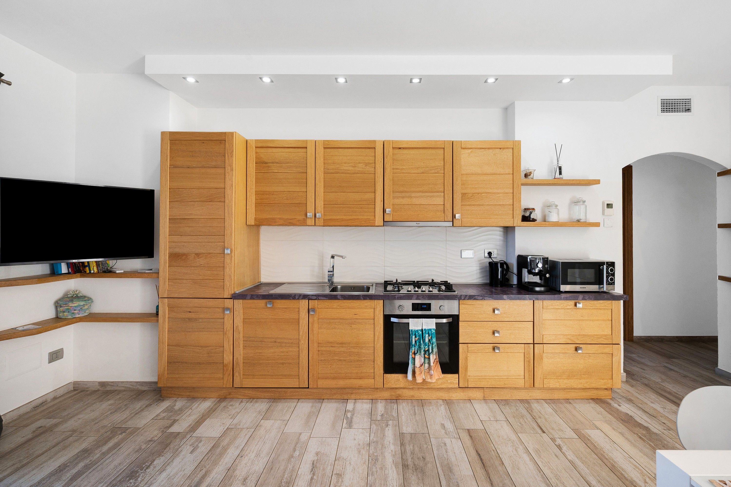 A modern kitchen with wooden cabinets, a built-in oven, a microwave, and a coffee machine.