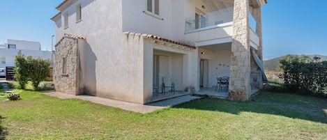 A two-story house with a balcony, a stone foundation, and a small garden.