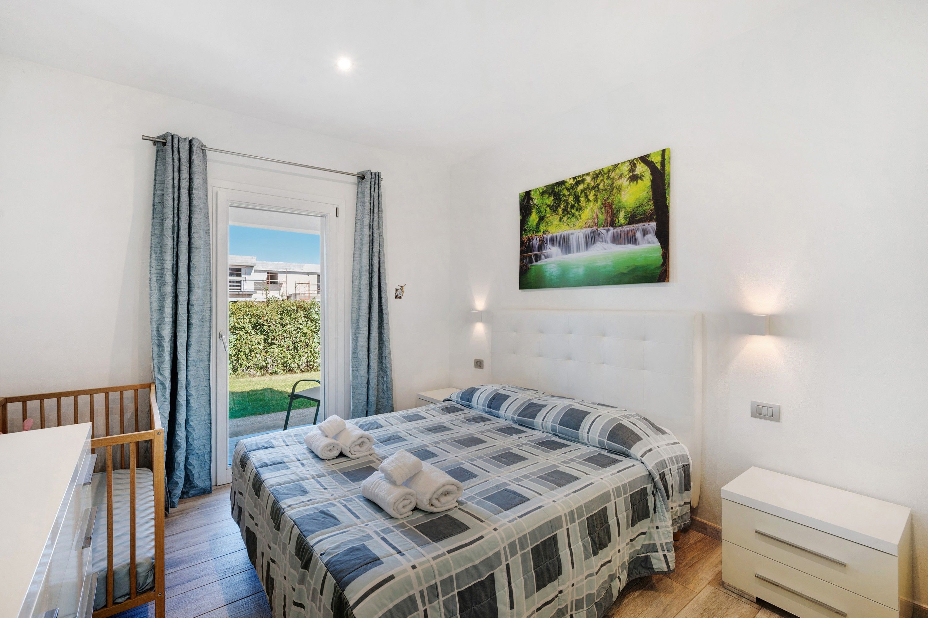 Une chambre à coucher avec un lit, un bureau, une chaise, une fenêtre avec des rideaux et un tableau accroché au mur.