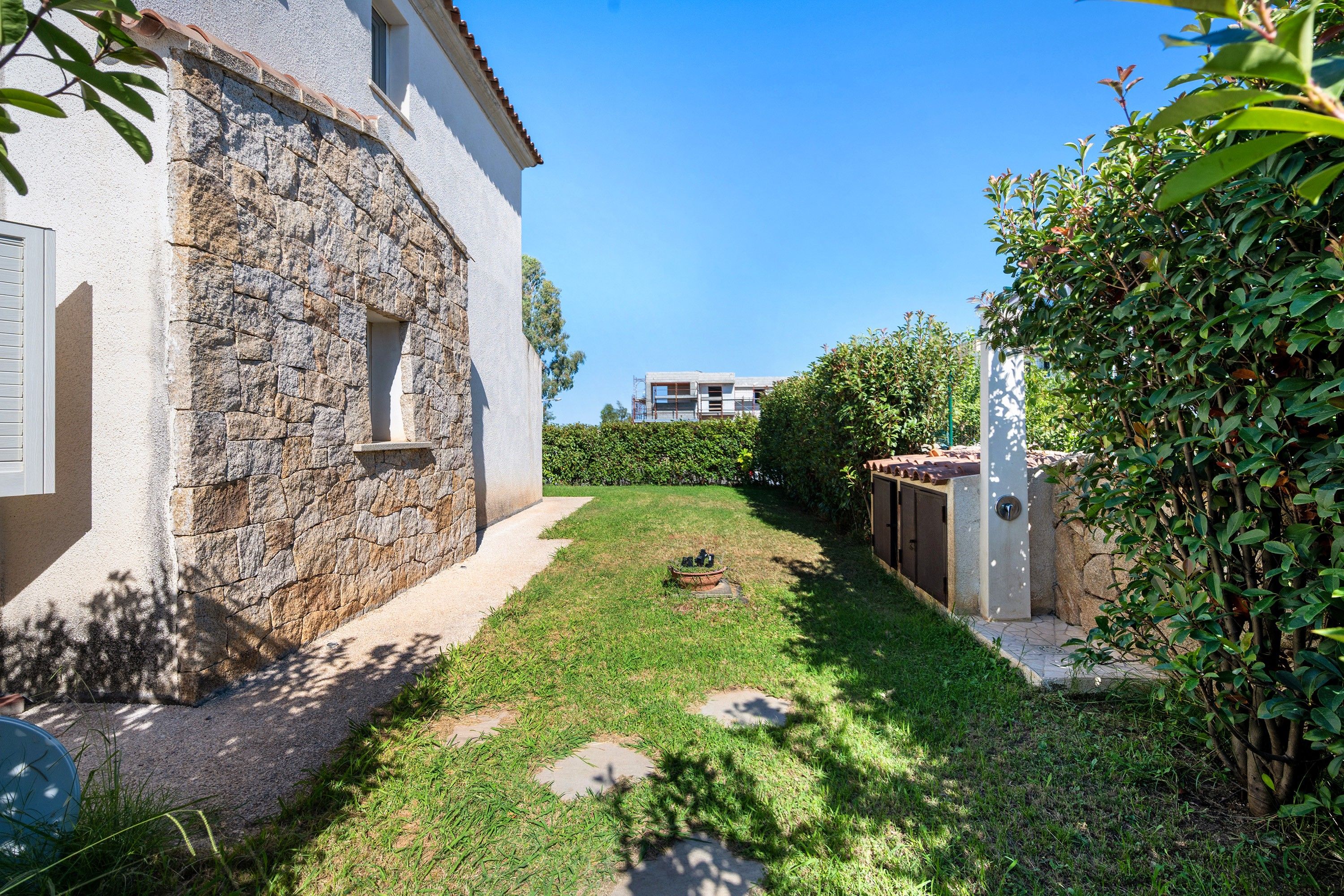 Un edificio in pietra con un piccolo giardino, un vialetto lastricato e un cielo azzurro intenso.